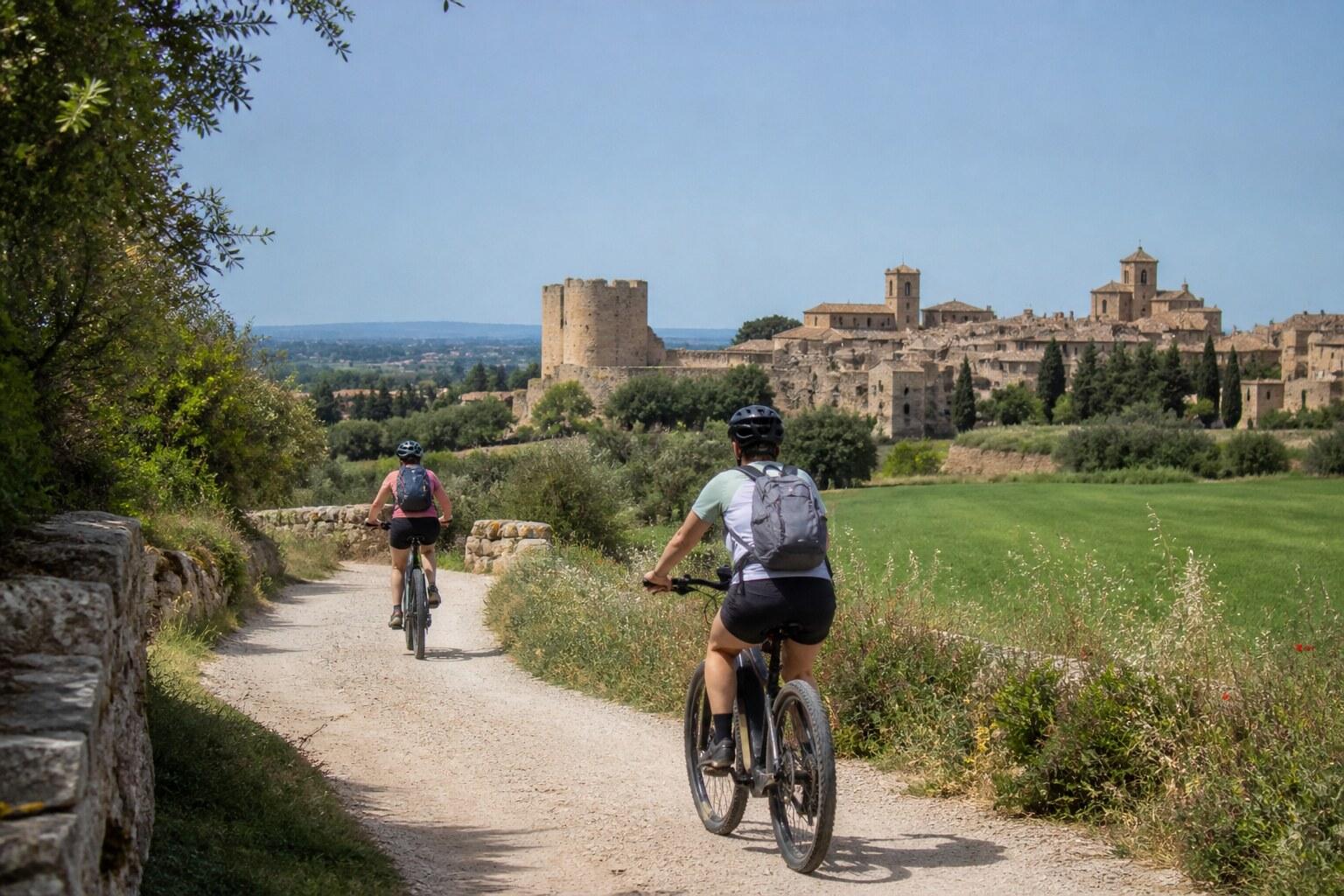 E-bike riders approaching a medieval Empordà village through fields