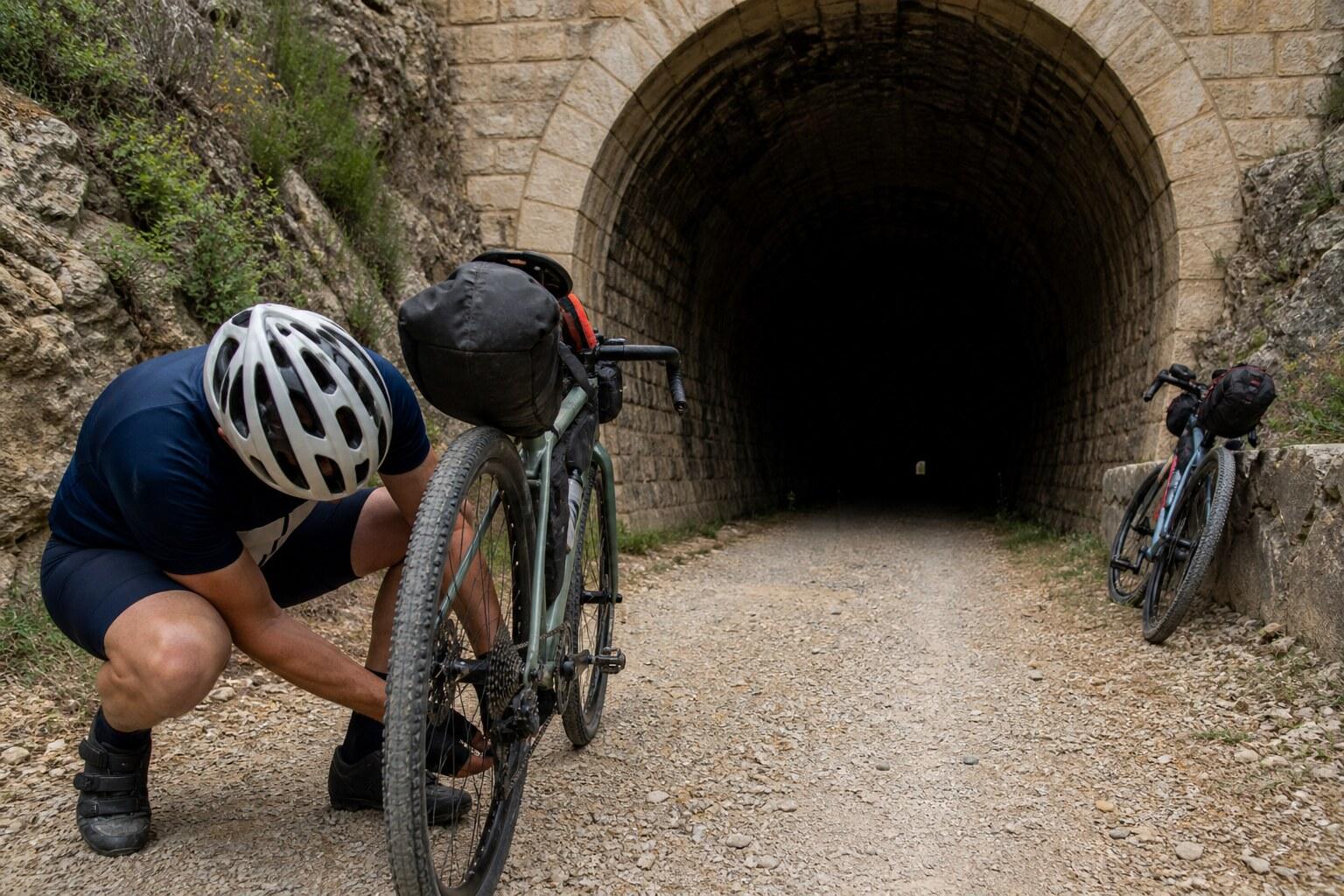 Cyclist repairing a bicycle beside a Terra Alta tunnel